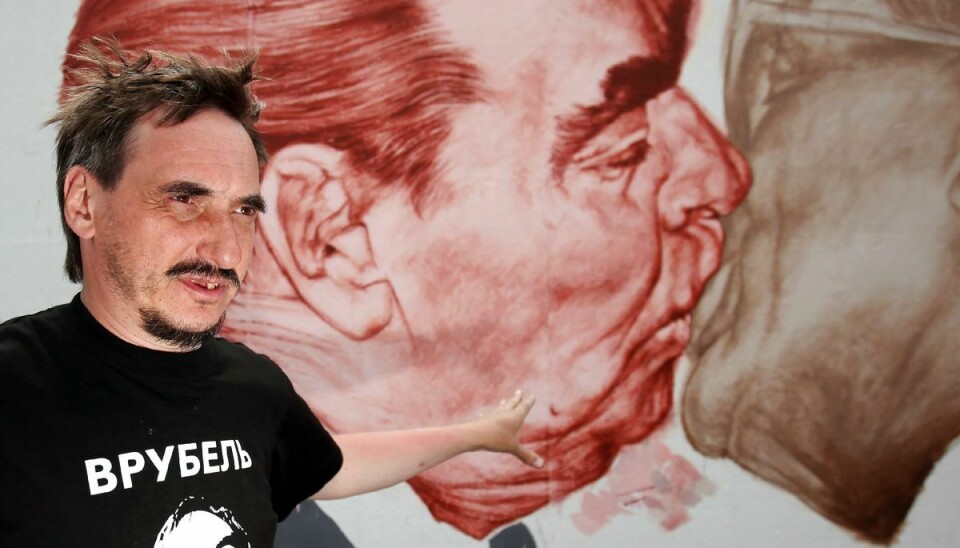Den russiske kunster Dmitri Vrubel, der her ses ved sit berømte værk på Berlinmuren i 2009, er død. Han blev 62 år.