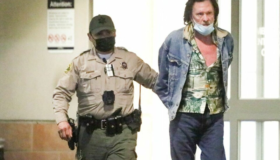 Michael Madsen, pacificeret med håndjern, føres bort af en politibetjent.