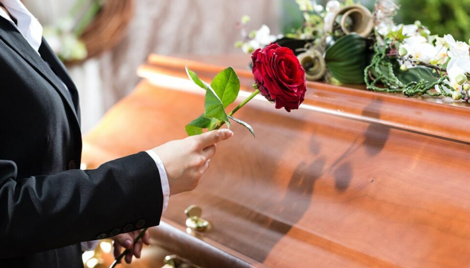 Mourning woman on funeral with red rose standing at casket or coffin