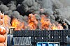 Flammer og sort røg over en industrihavn med containere i forgrunden.