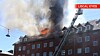 Røg og ild stiger op fra taget på en bygning, mens en brandstige peger mod den øverste etage.